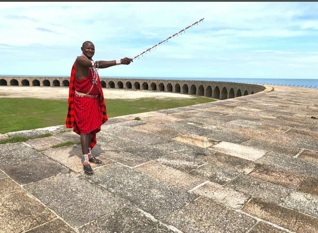 Participant en tenue maasai rouge sur le rempart du fort, devant la batterie circulaire